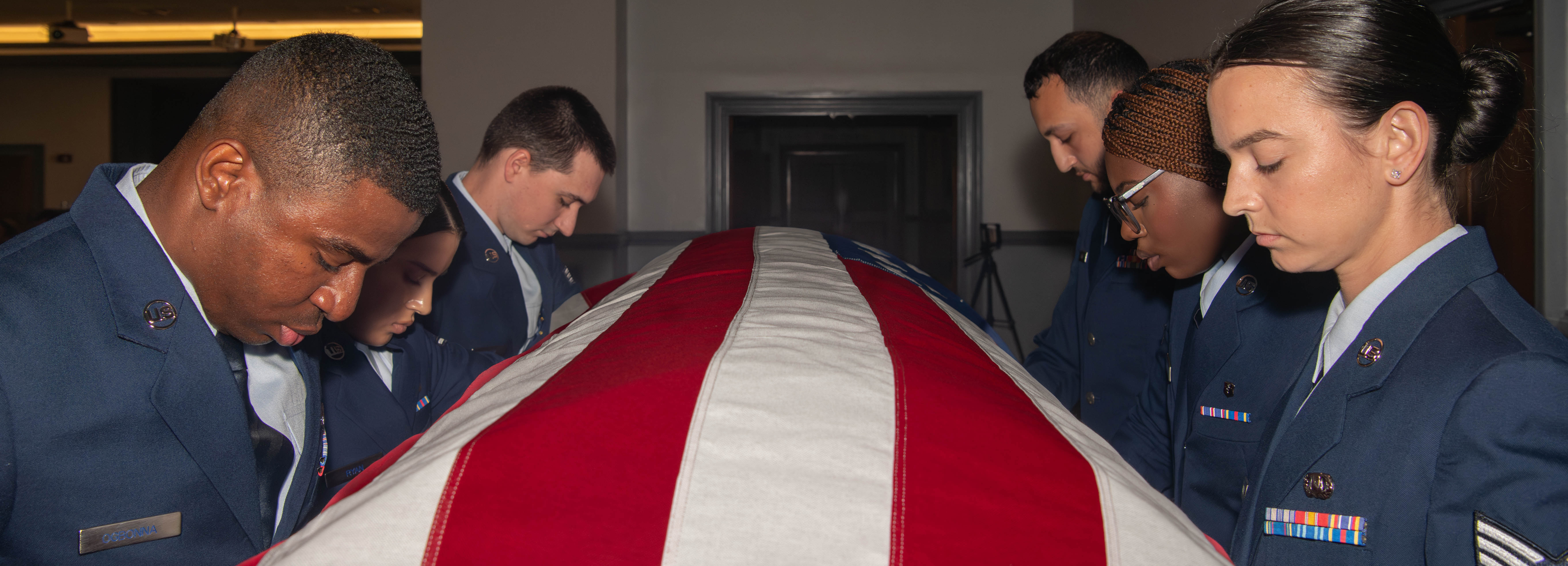 A photo of six Airmen holding up a casket.