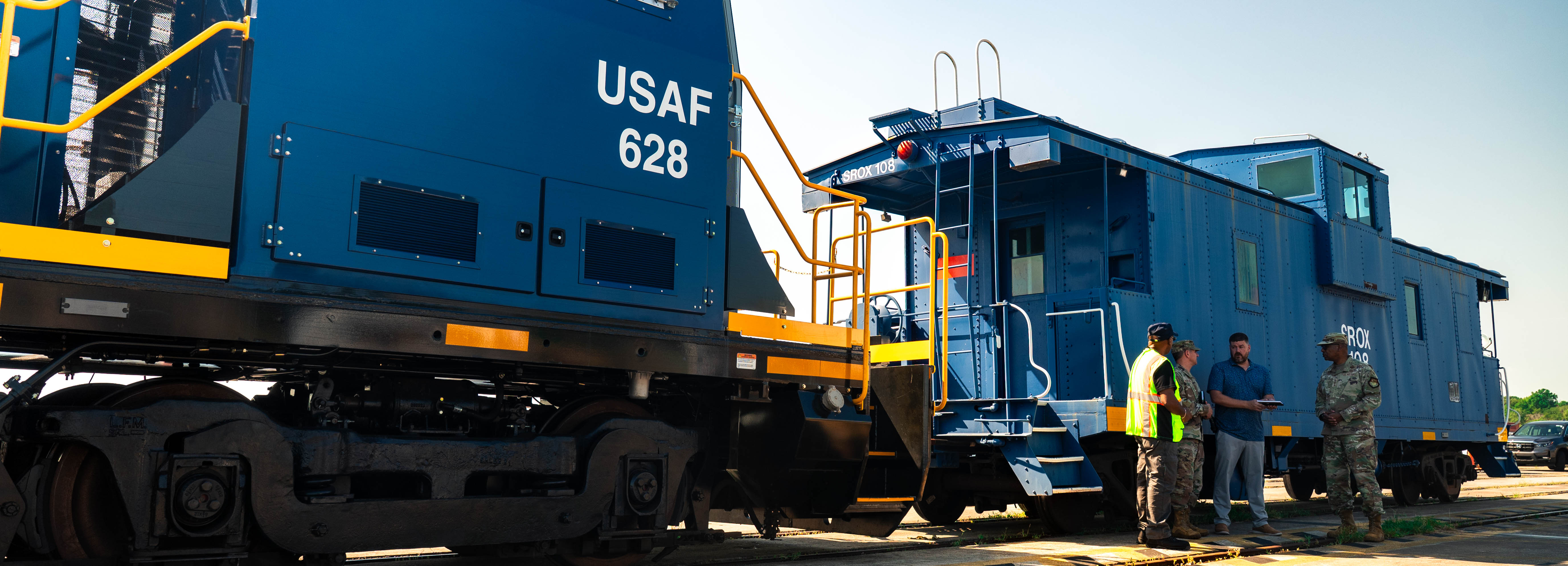 A photo of four people conversing in front of a locomotive