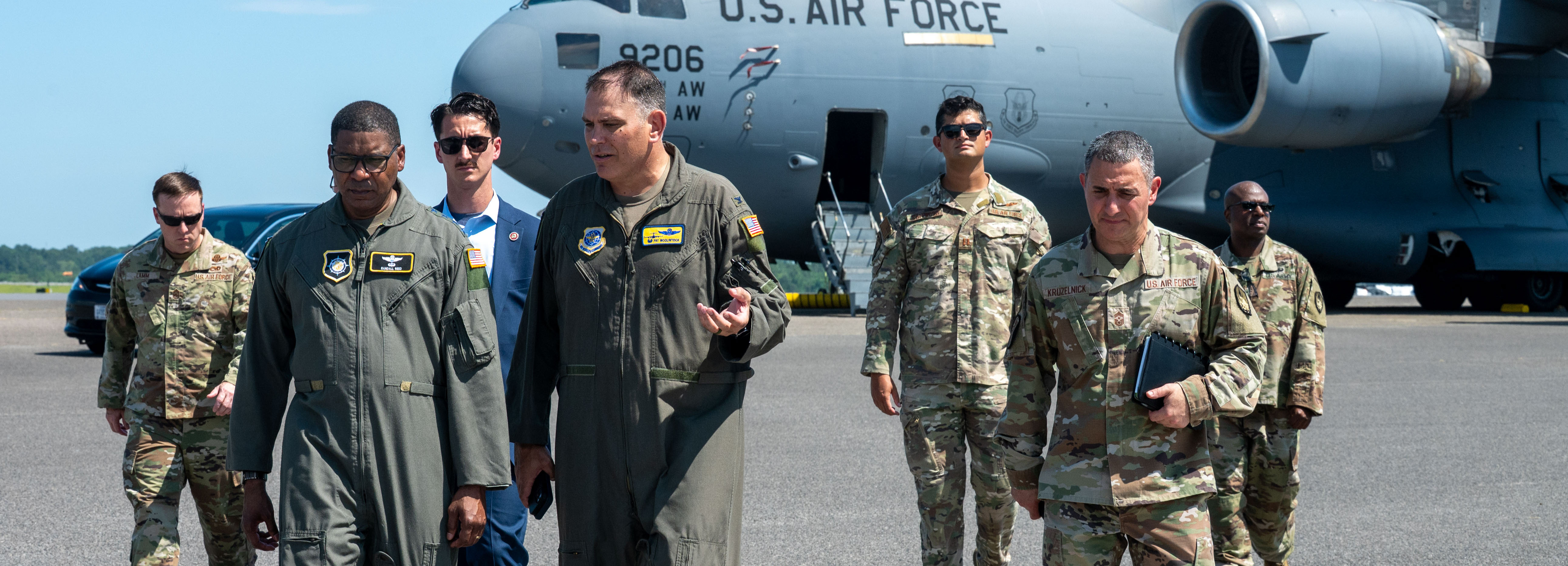 Leadership in various uniforms walk away from an aircraft on the flightline.