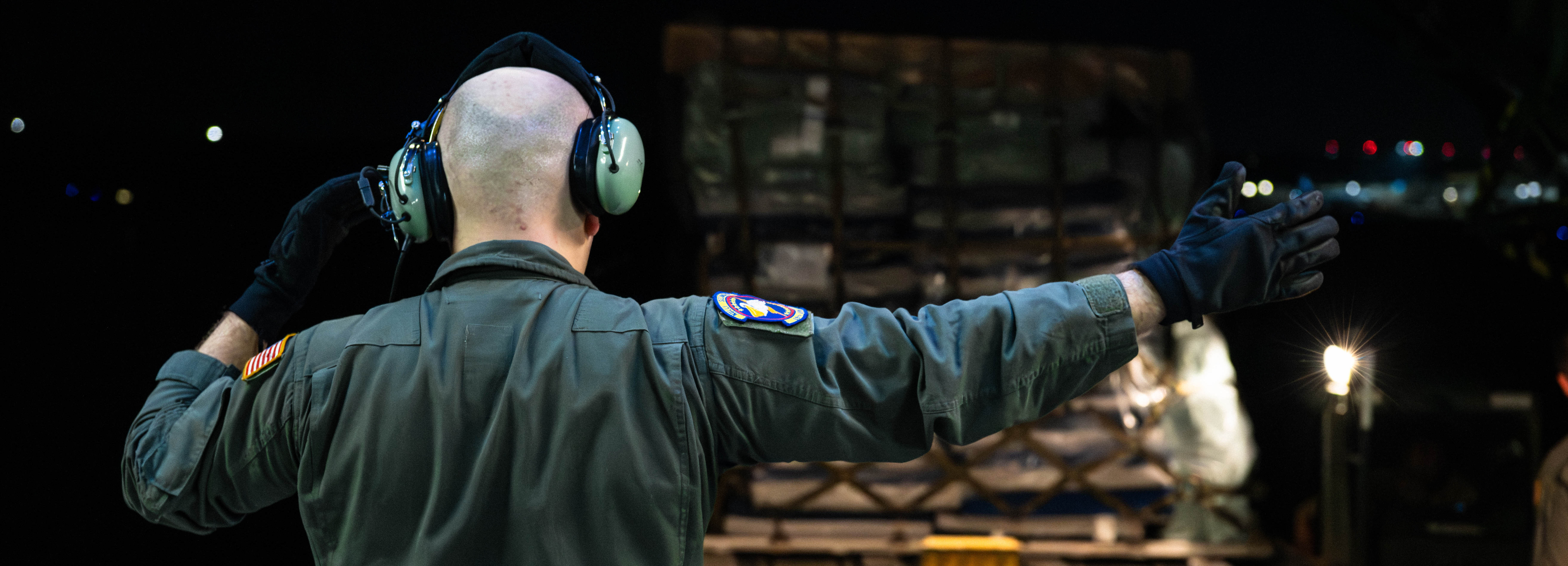An Airman gestures to the right, directing a pallet of cargo being loaded onto an aircraft.