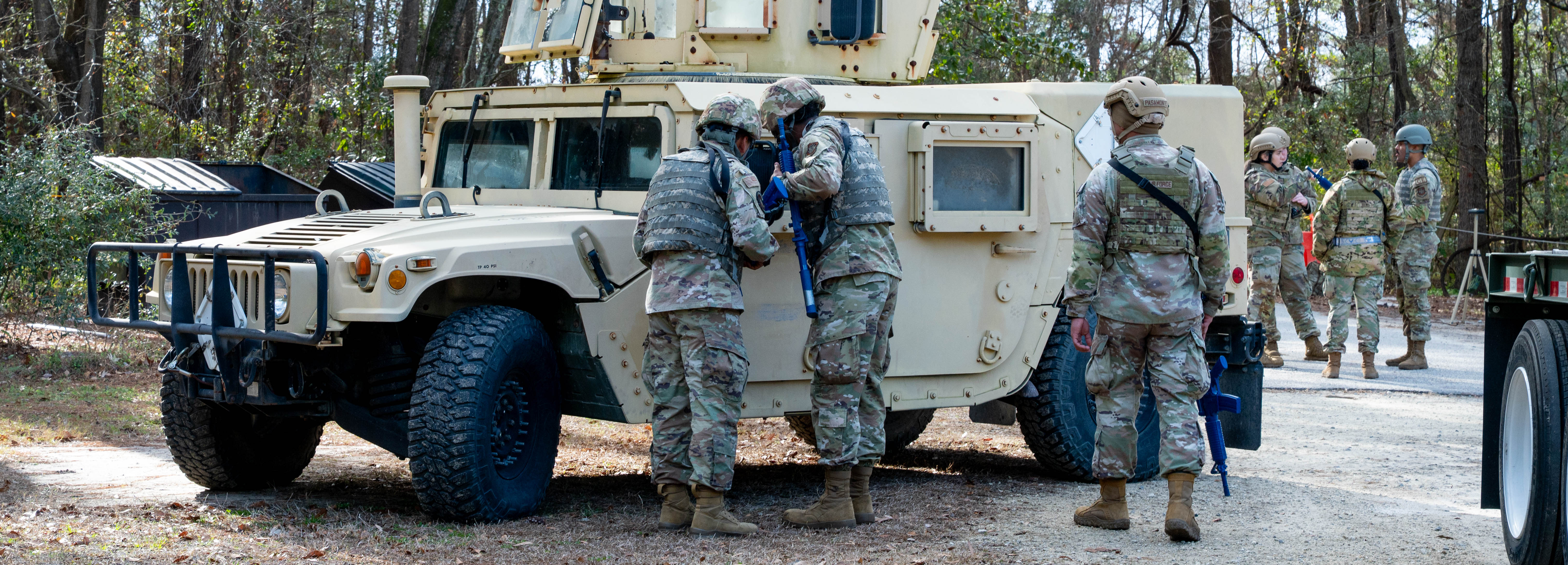 Three Airmen stand around a tan Humvee
