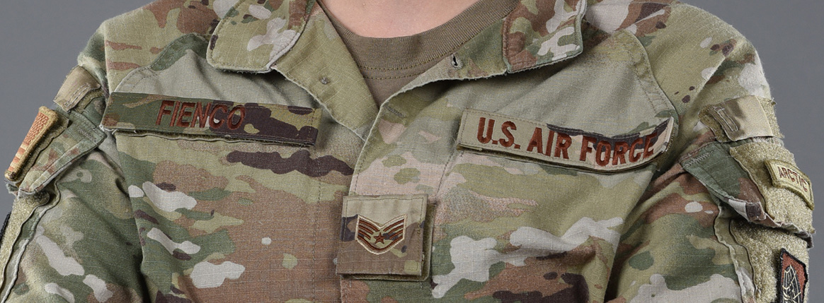 An Airman stands in front of a grey background with her arms crossed 